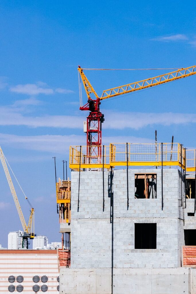 Tower cranes at a construction site working on a high-rise building under a clear blue sky.
