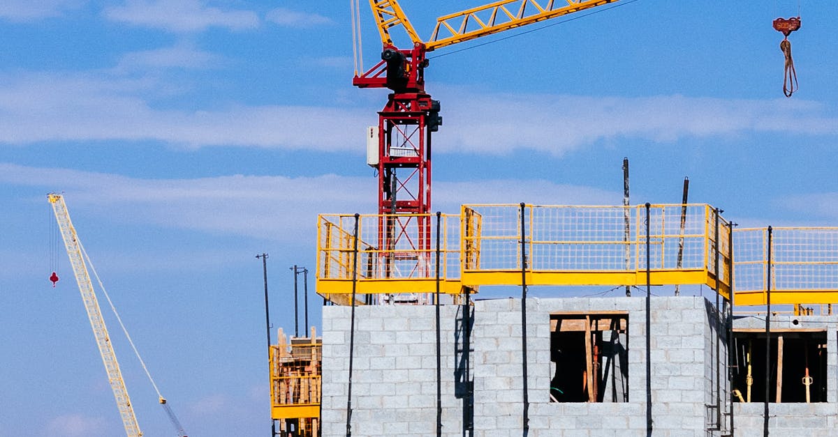 Tower cranes at a construction site working on a high-rise building under a clear blue sky.